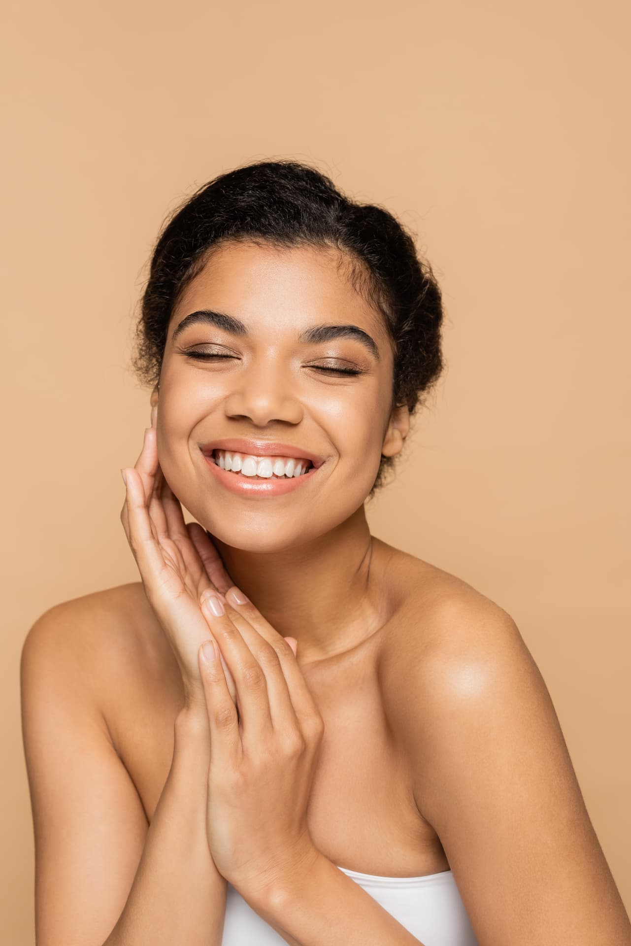 Smiling woman with smooth, radiant skin resting her hands near her face