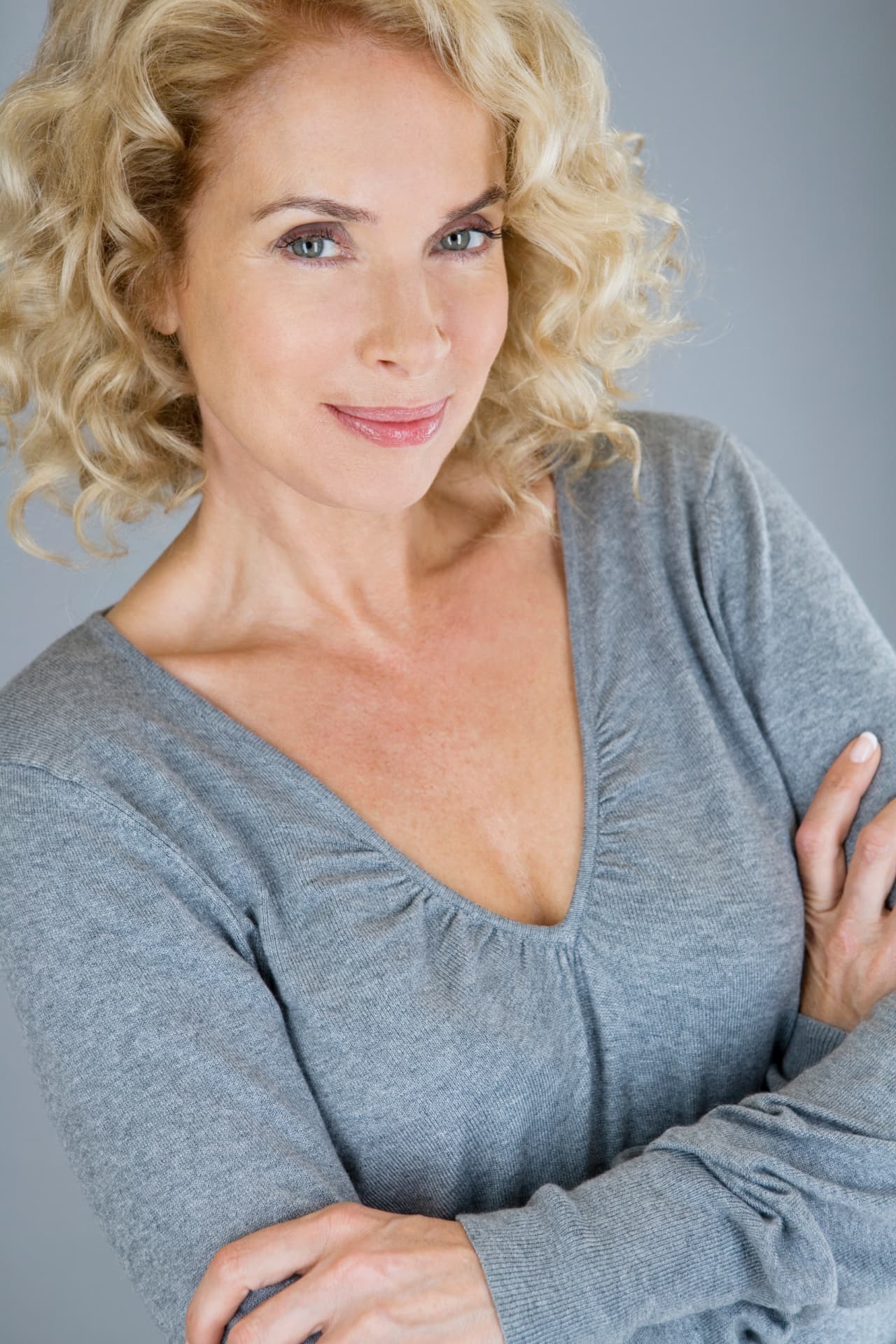 Woman with curly blonde hair in a grey sweater, calm and confident