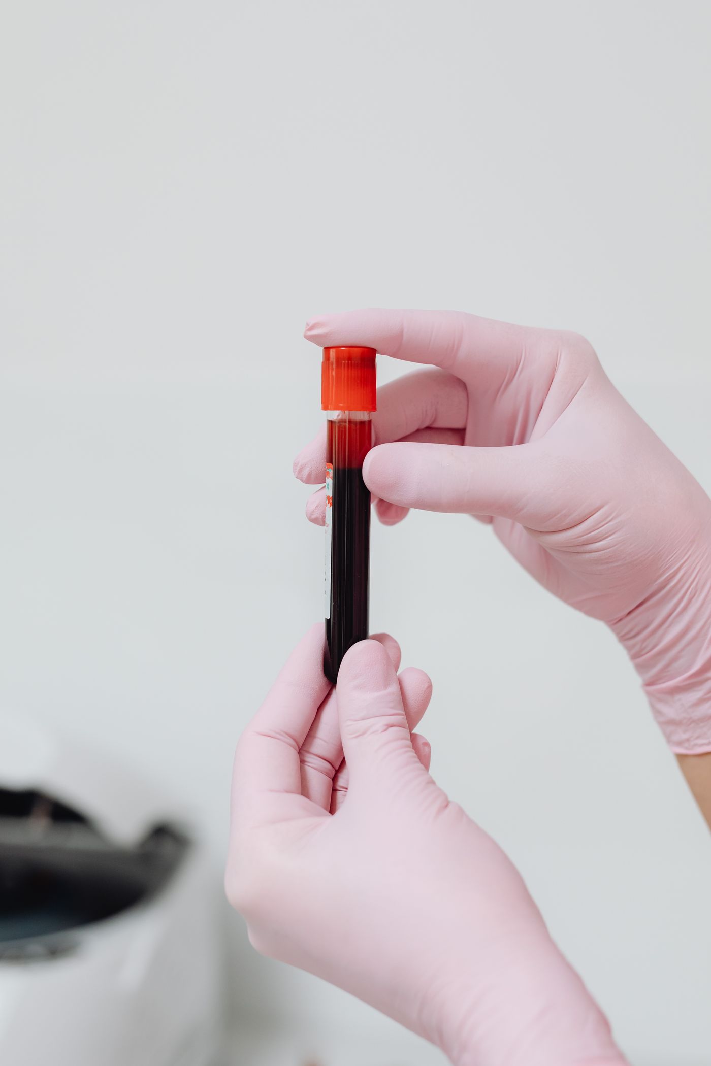 Gloved hands holding a sealed specimen tube against a plain neutral background