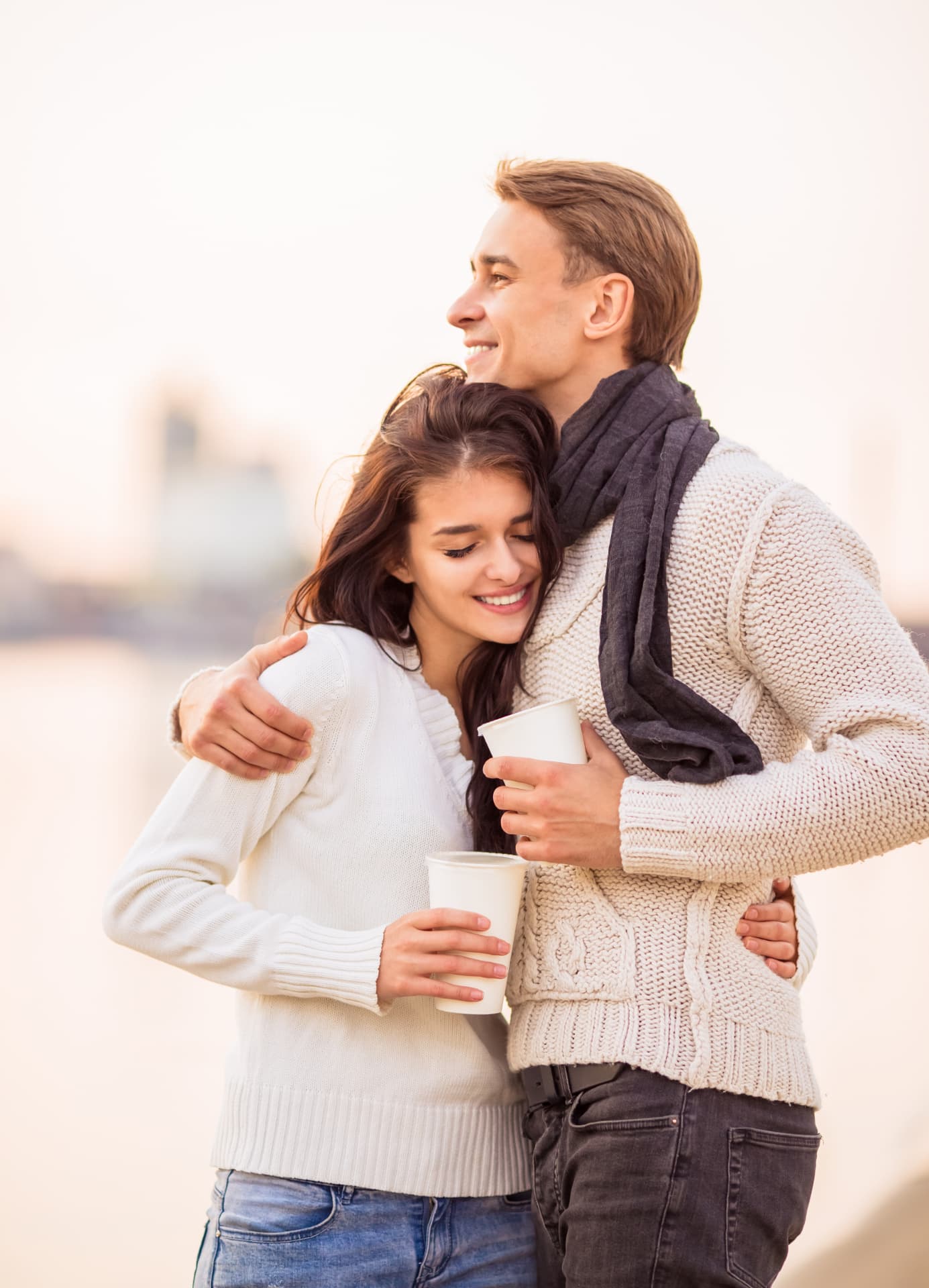 Couple embracing outdoors holding coffee cups in warm light