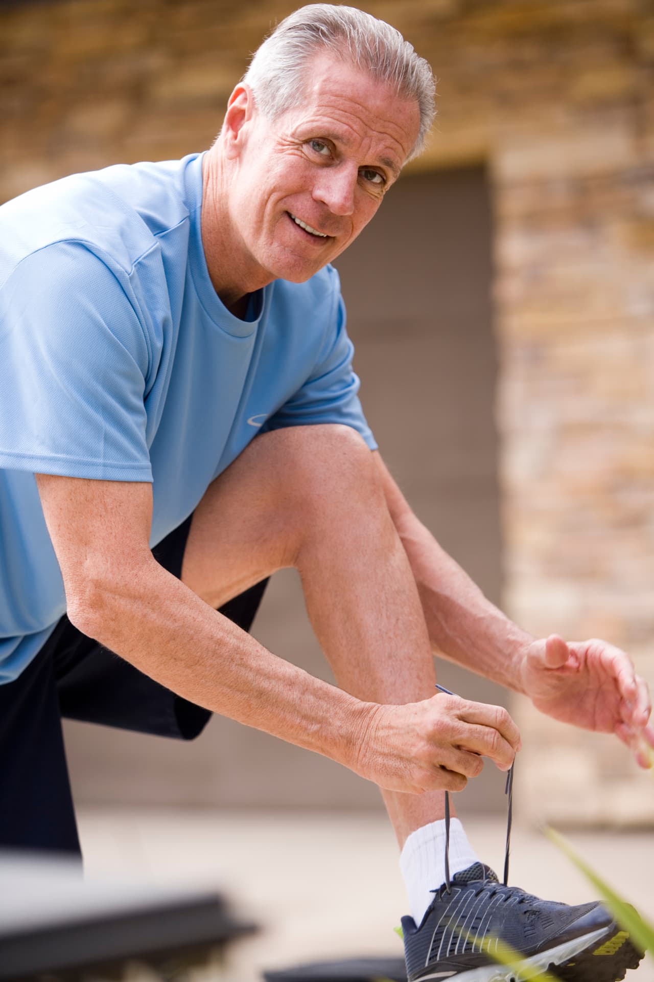 Older man in a blue athletic shirt tying his running shoe outdoors