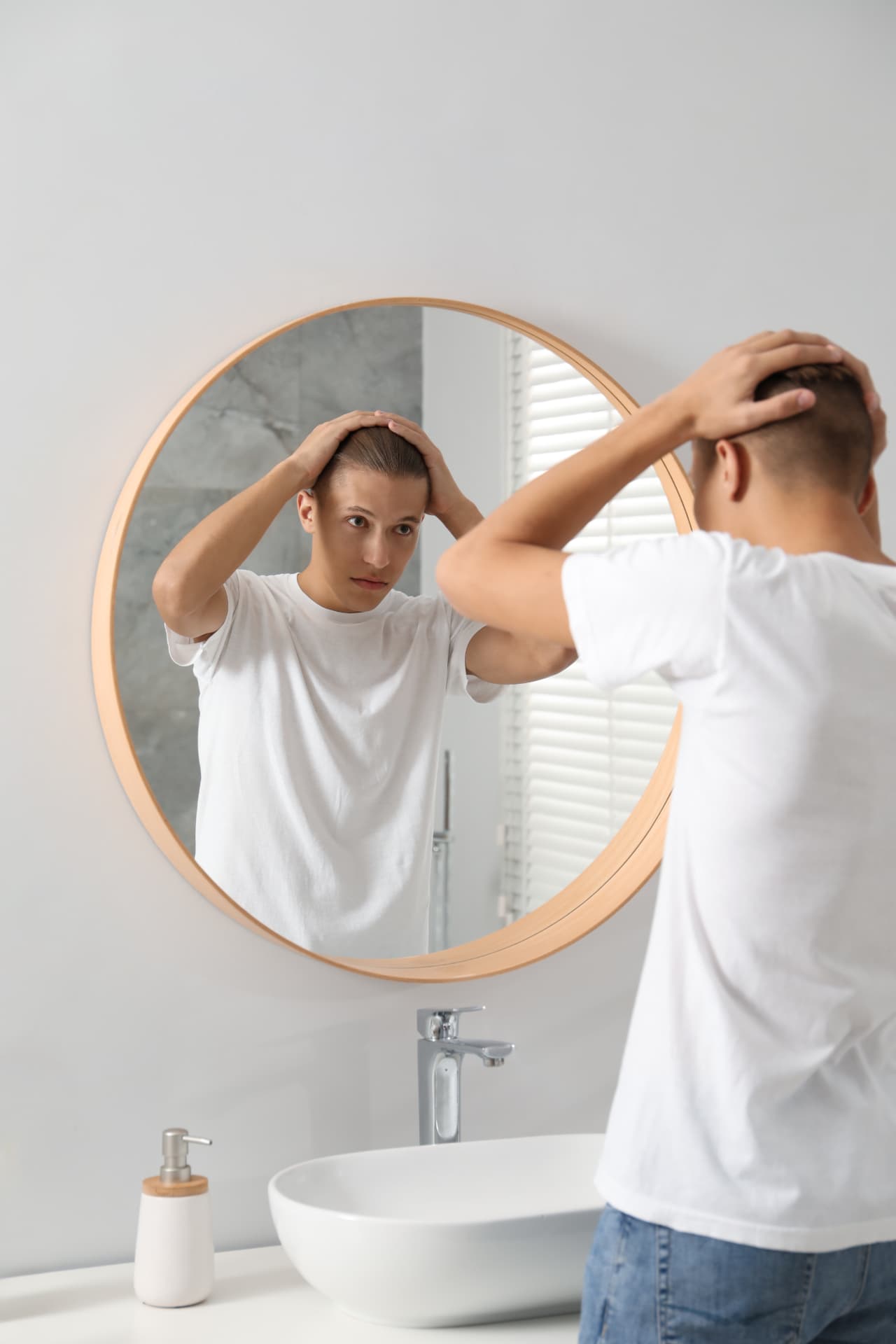 Young man examining his hairline in a bathroom mirror