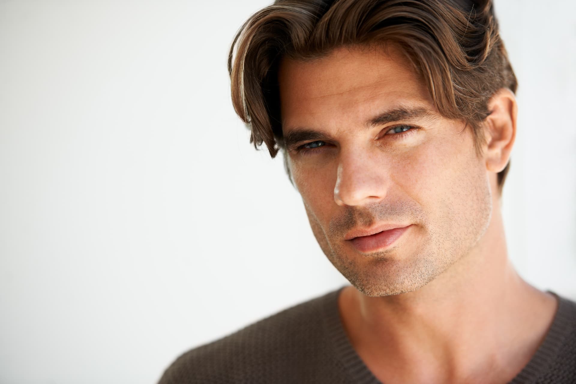Man with full brown hair in a brown sweater against a light indoor backdrop