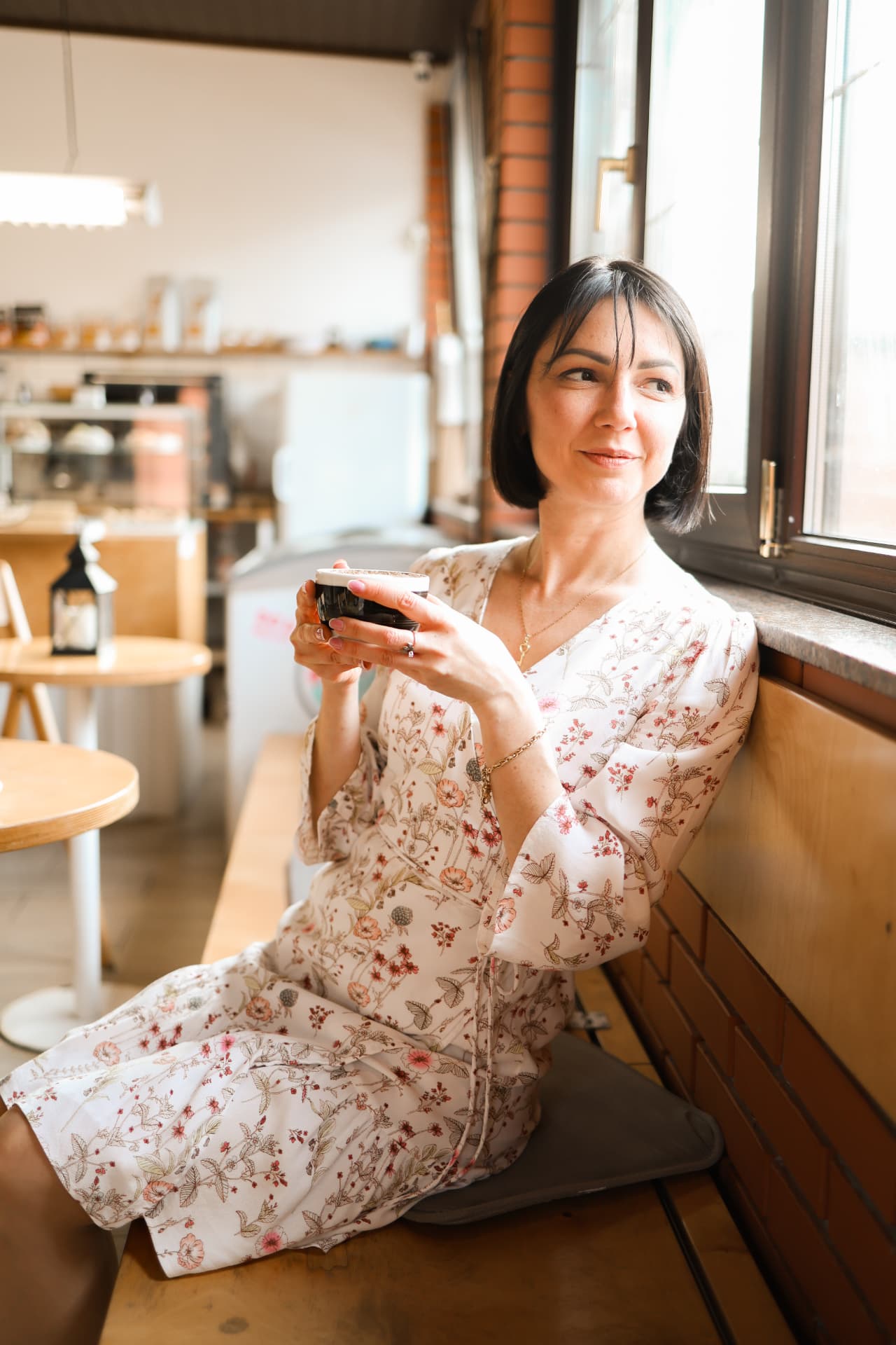 Woman with short dark hair enjoying coffee in a sunlit cafe